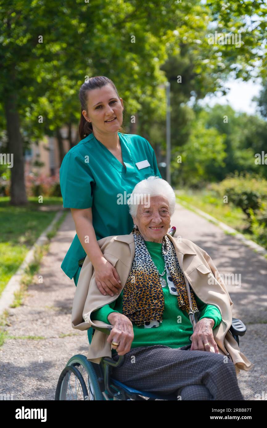 An elderly woman with the nurse on a walk in the garden of a nursing home in a wheelchair Stock Photo