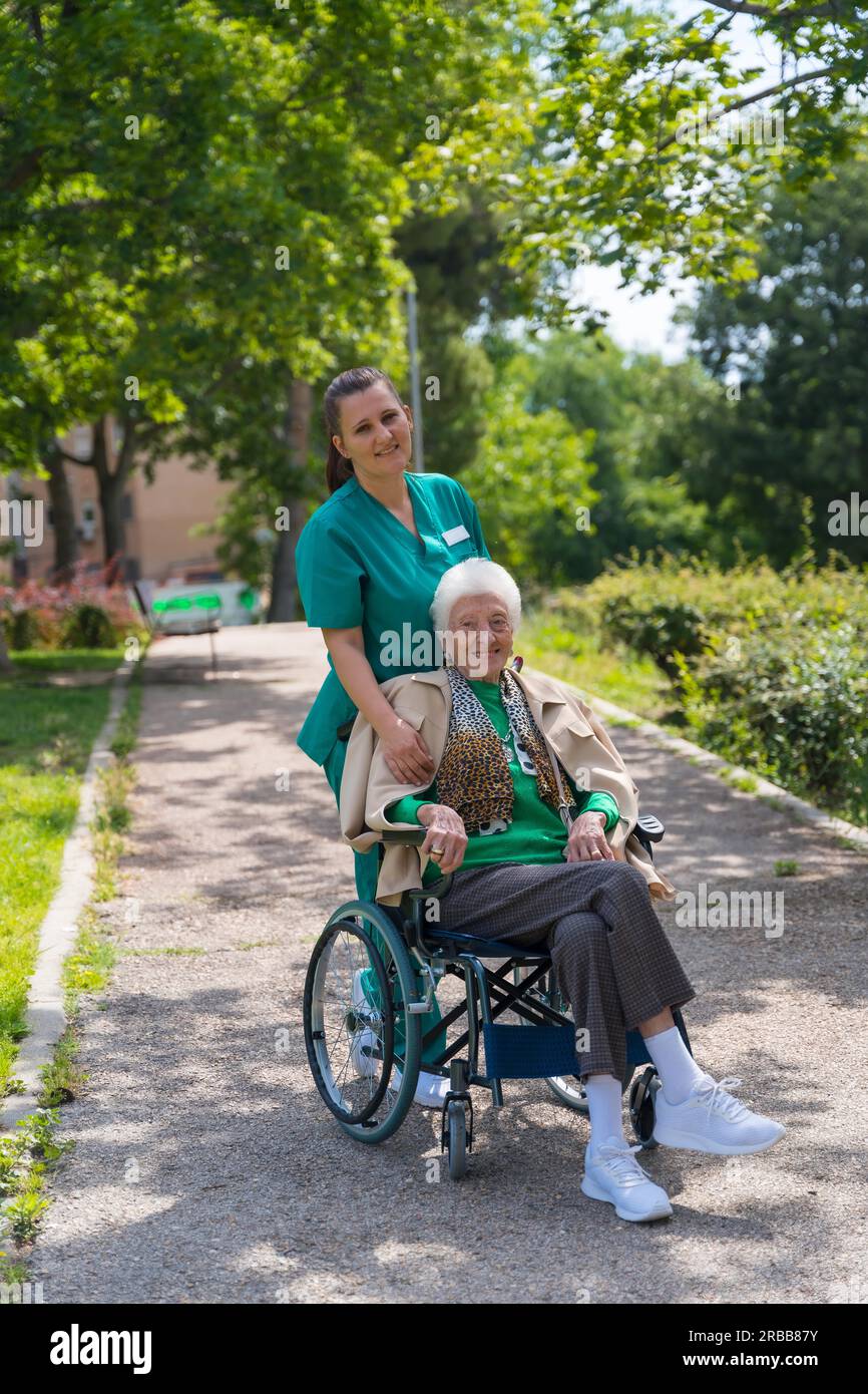 Portrait of an elderly woman with the nurse on a walk in the garden of a nursing home in a wheelchair Stock Photo