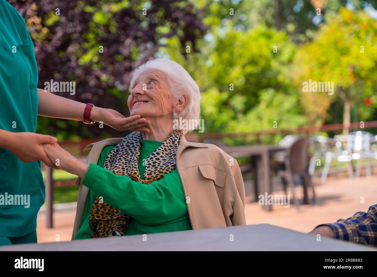 An older or mature woman with the nurse in the garden of a nursing home in a moment of affection Stock Photo