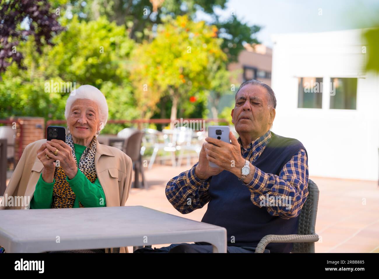 Two very happy elderly people in the garden of a nursing home, looking at the phone, technologies in the elderly Stock Photo