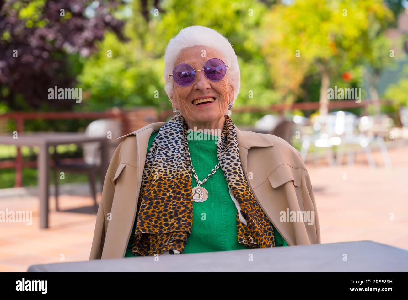 An elderly woman smiling in the garden of a nursing home or retirement home at a summer party wearing sunglasses Stock Photo