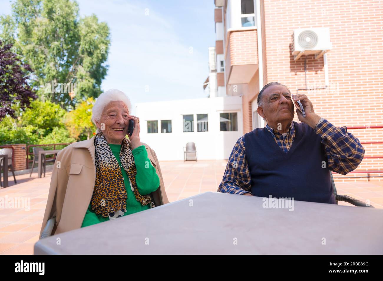 Two elderly people in the garden of a nursing home, looking at the phone, technologies in the elderly Stock Photo