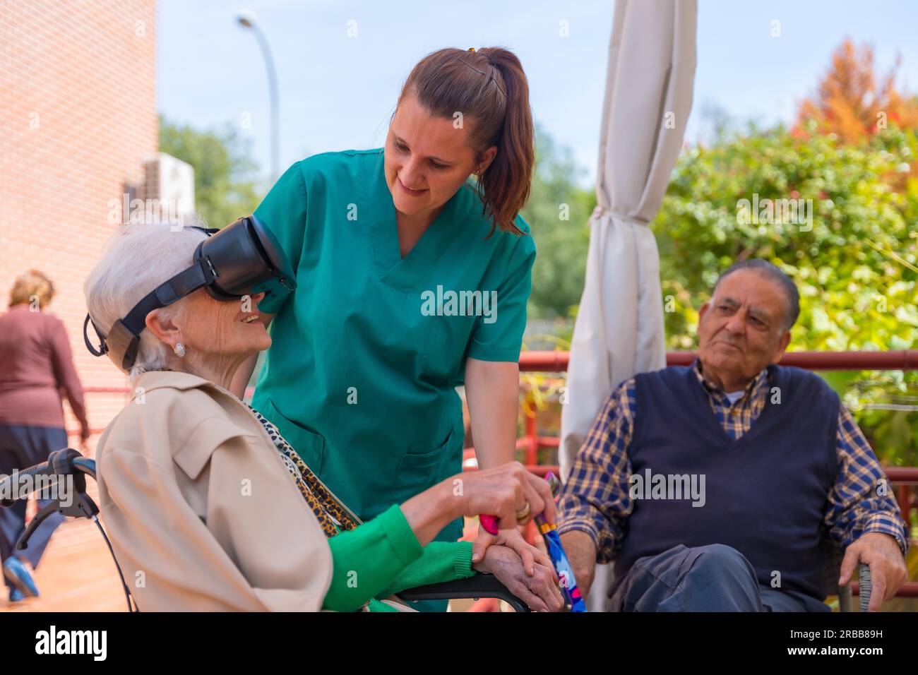 An elderly woman with the nurse looking through virtual reality glasses in the garden of a nursing home, vr glasses with the smiling Stock Photo