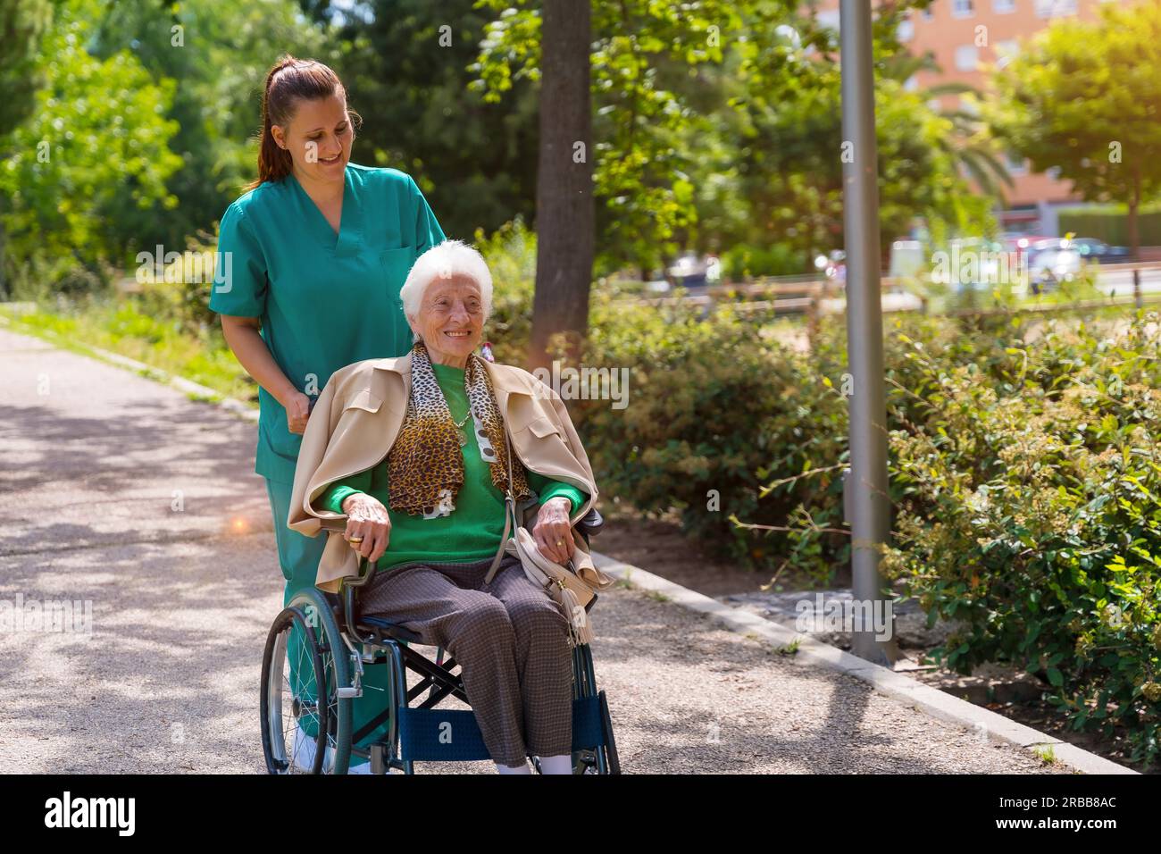 An elderly woman with the nurse on a walk in the garden of a nursing home in a wheelchair next to nature Stock Photo