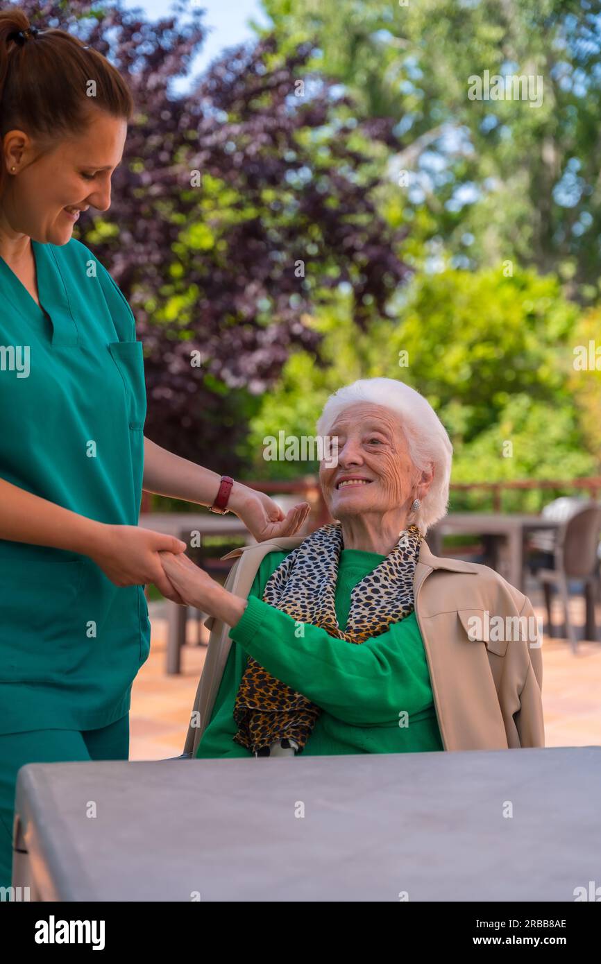 An older or mature woman with the nurse in the garden of a nursing home in a moment of love and affection Stock Photo