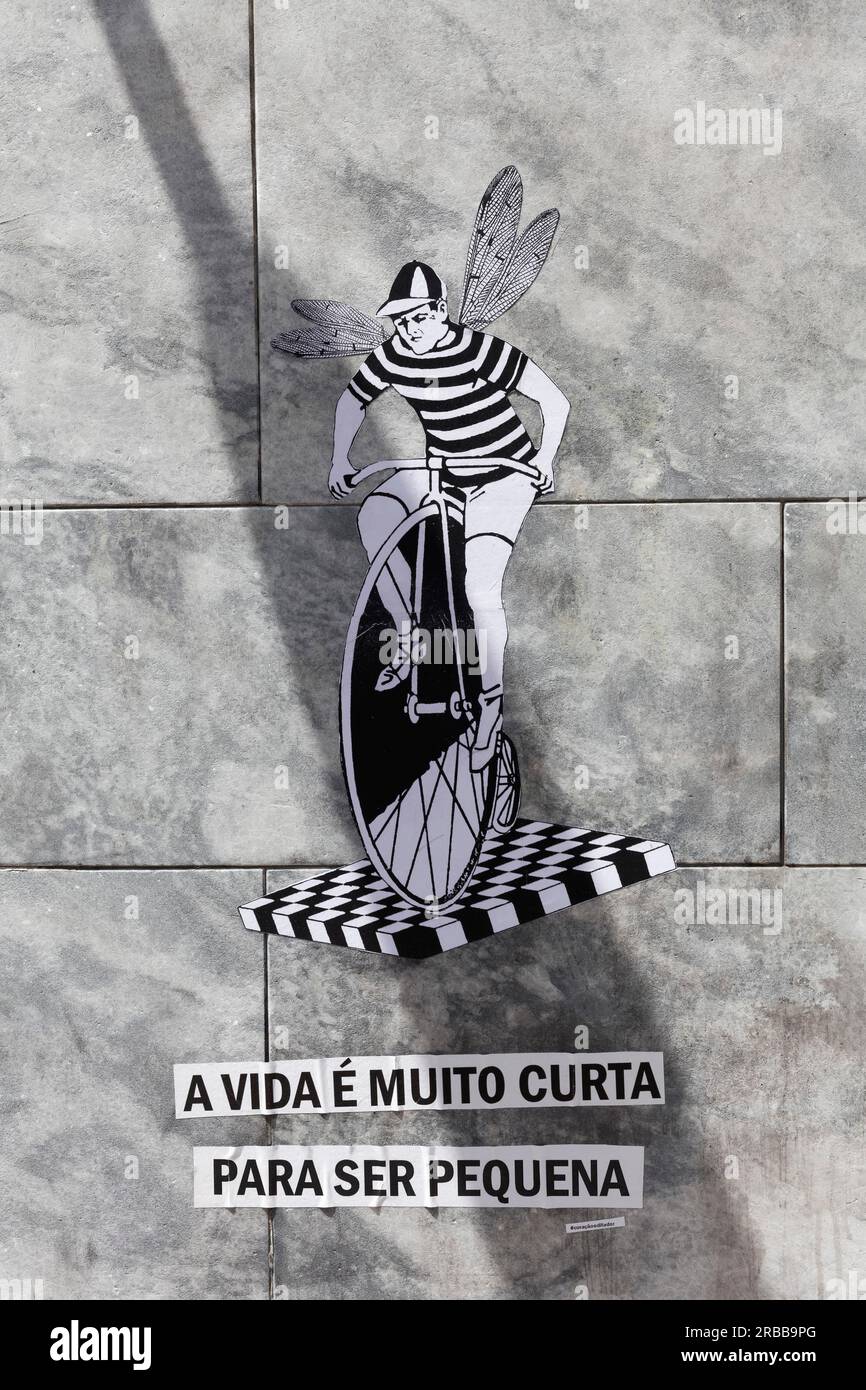 Funny paste-up, man with wings riding a penny-farthing, saying in Portuguese Life is too short to be small, street art, Porto, Portugal Stock Photo