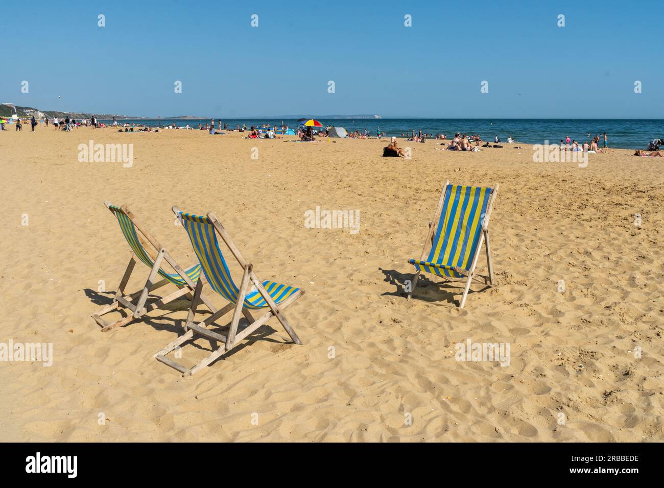 Bournemouth, UK - July 7th 2023: Three lonely deck chairs on Bournemouth beach with sunbathers and sea in the background. Stock Photo