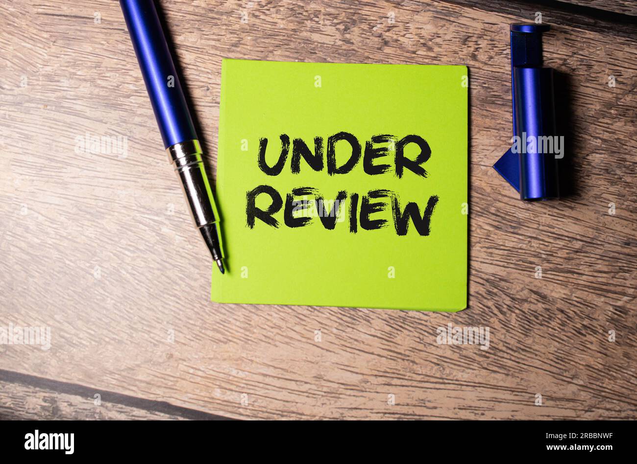 Under Review. text on white paper. the inscription on the notebook. business concept. notepad on a wooden background. glasses, pen, pencil Stock Photo