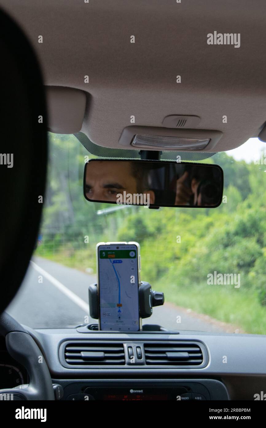 Adult male driving rented car in Mallorca island using smartphone gps for orientation. Searching beaches, cales in Mallorca island. Stock Photo