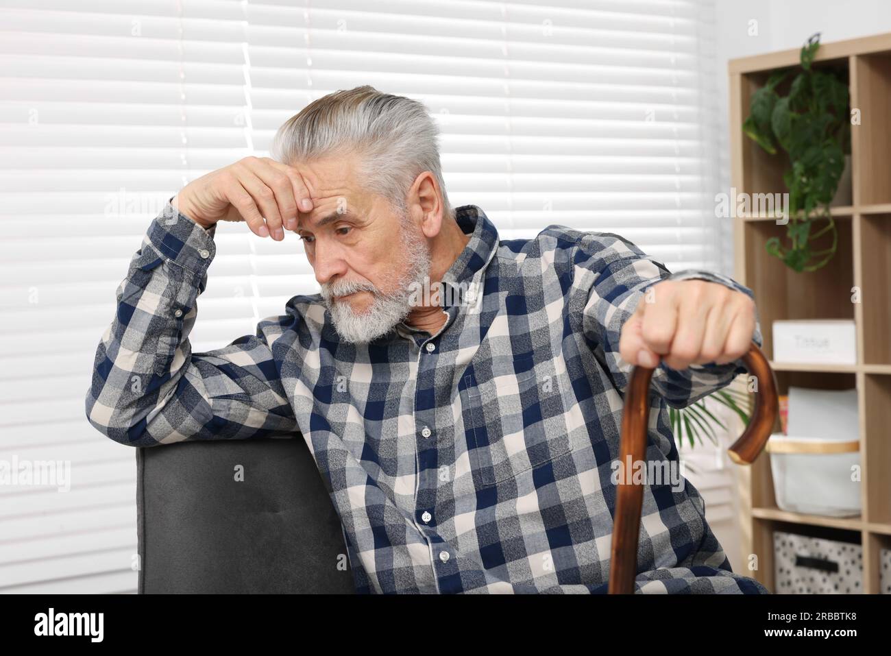 Senior man with walking cane sitting on armchair at home Stock Photo ...