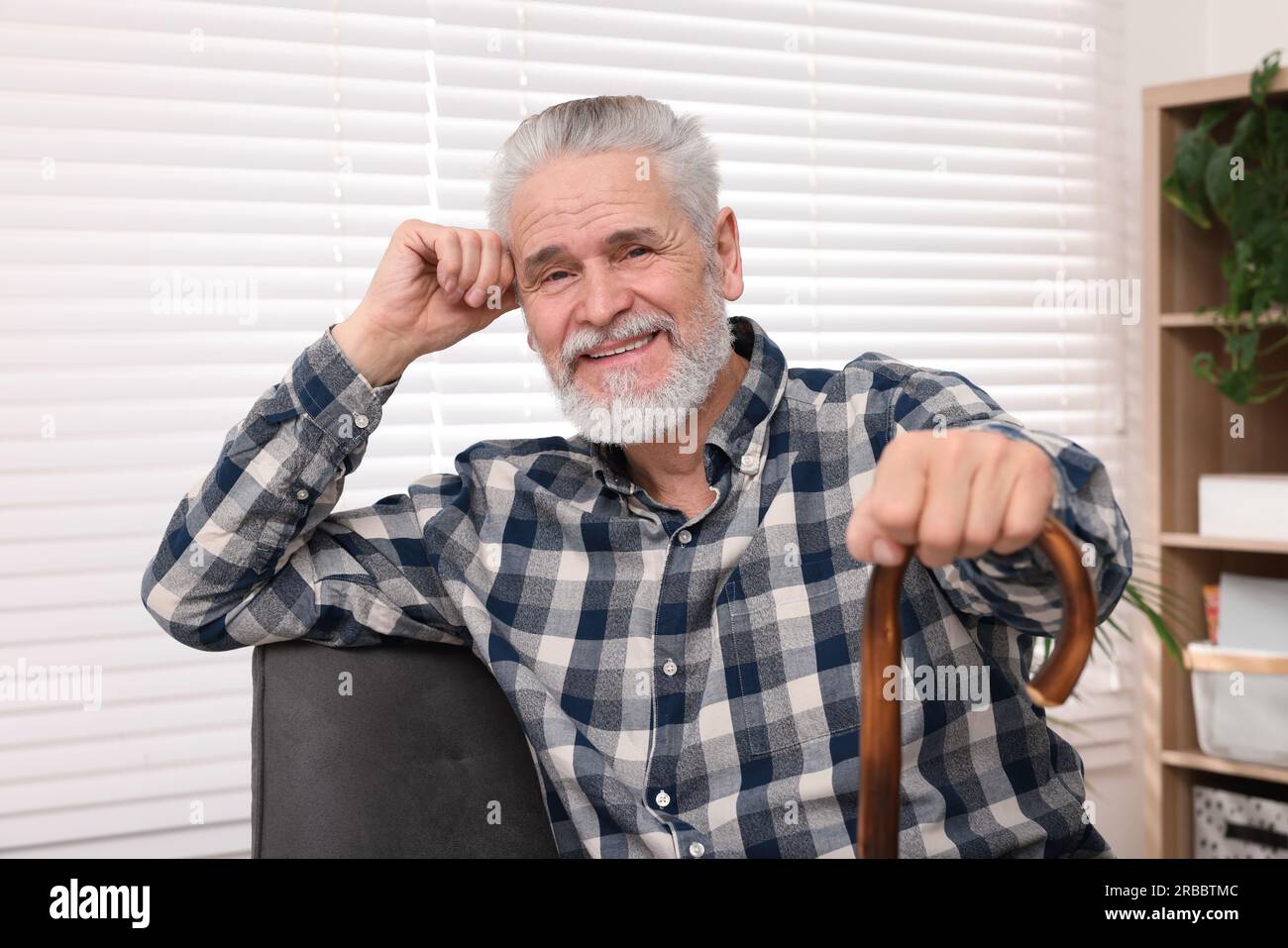 Senior man with walking cane sitting on armchair at home Stock Photo ...