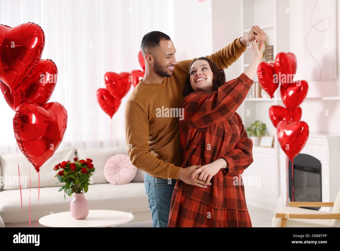 Lovely couple dancing in room decorated with heart shaped air balloons ...