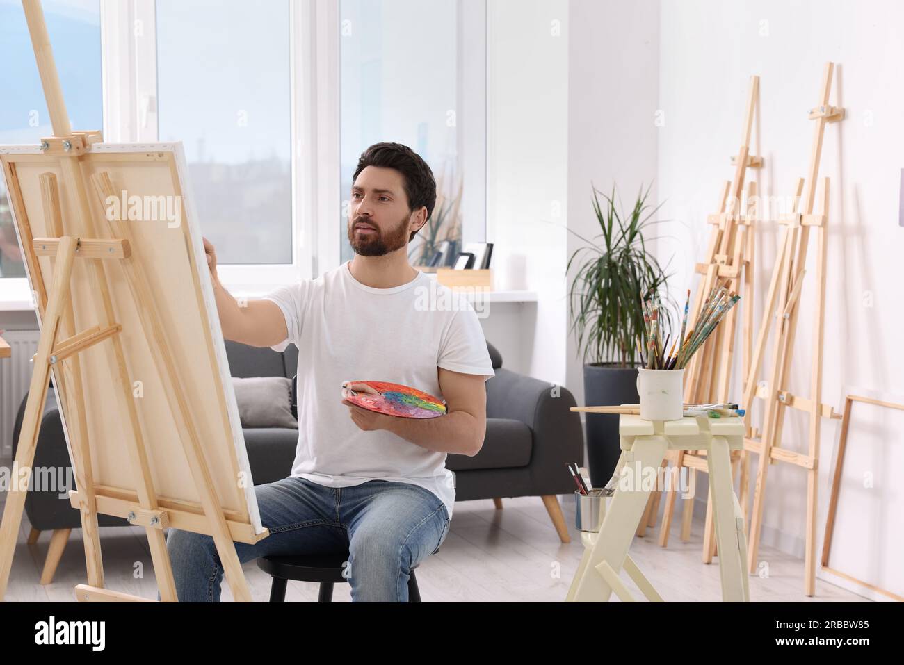 Man painting in studio. Using easel to hold canvas Stock Photo - Alamy