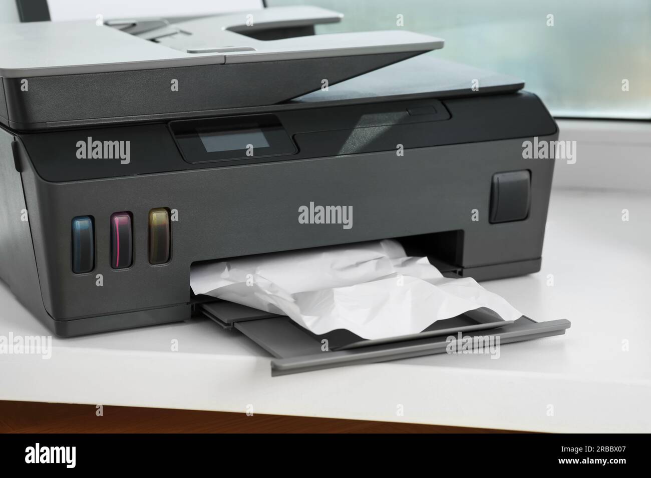 Modern printer with crumpled sheet of paper on window sill indoors