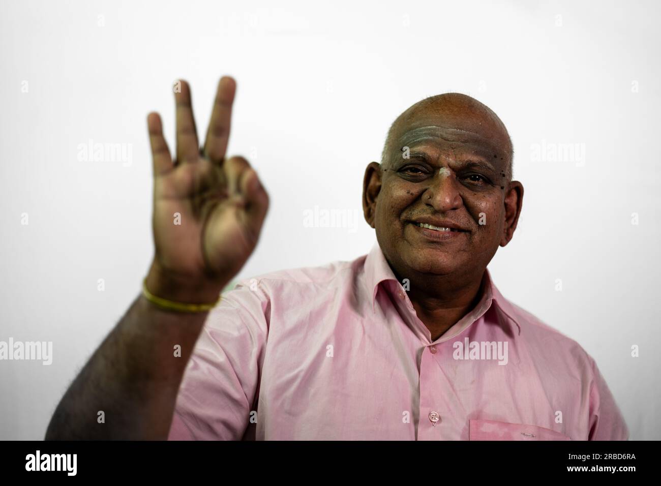 A South Indian old man with a bold expression says 'super' in front of the camera. His finger is out of focus in the foreground, creating a sense of d Stock Photo