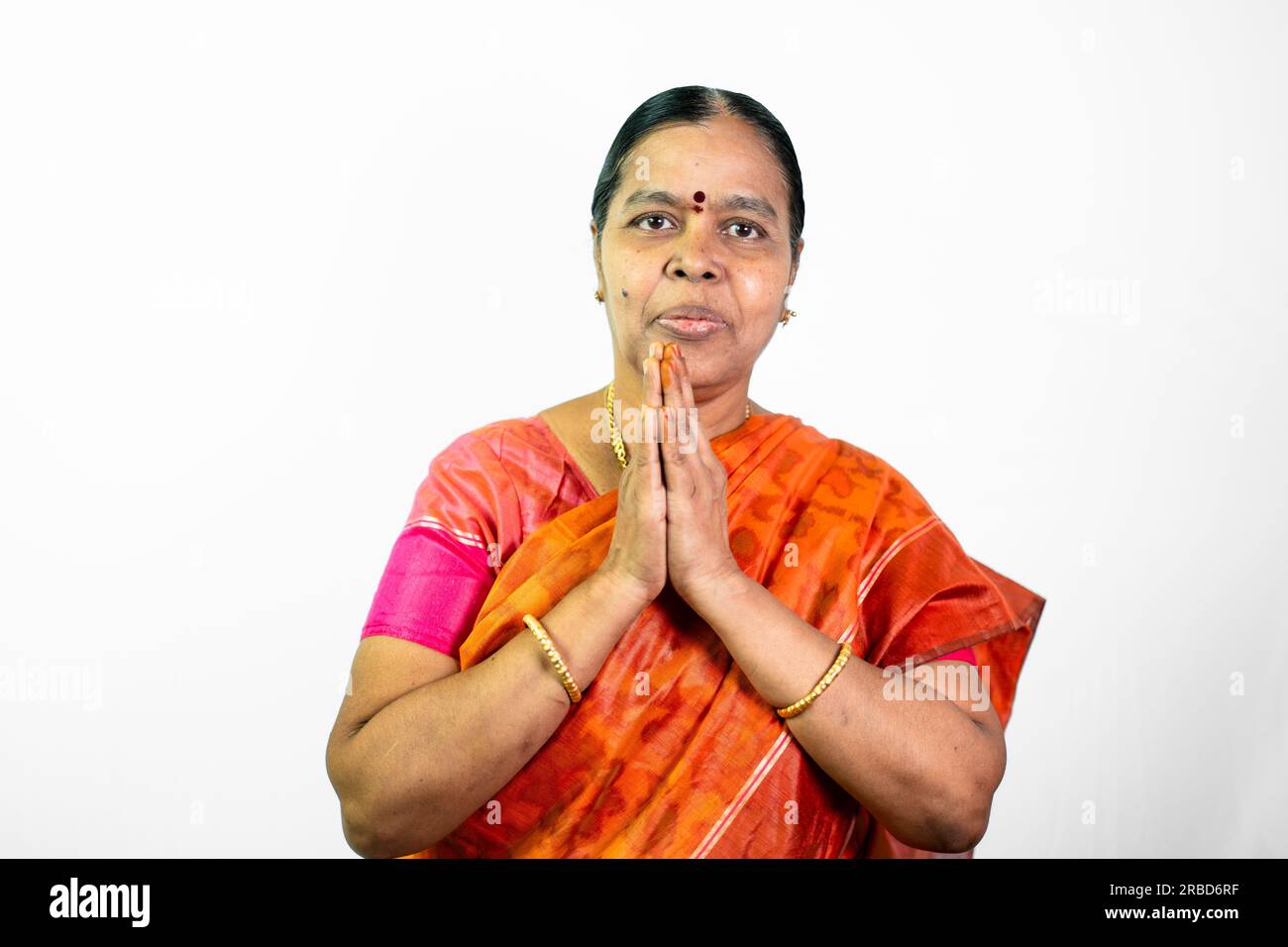 A beautiful South Indian woman in traditional attire is saying 'vanakkam' (hello) in Tamil. She is standing against a white background, and her hands Stock Photo