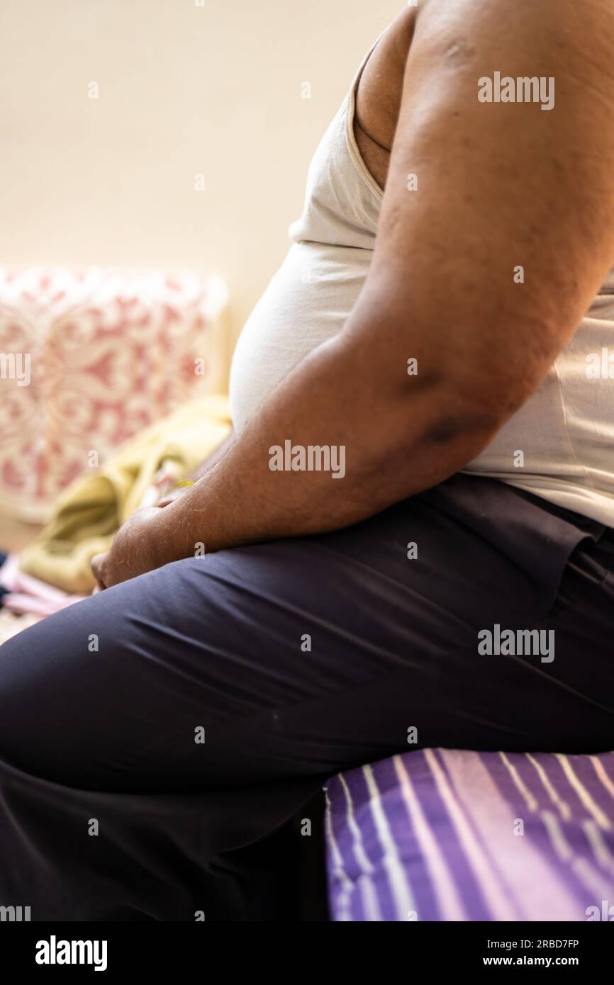A stock photo of a fat man sitting on a sofa, focused on his belly. Stock Photo