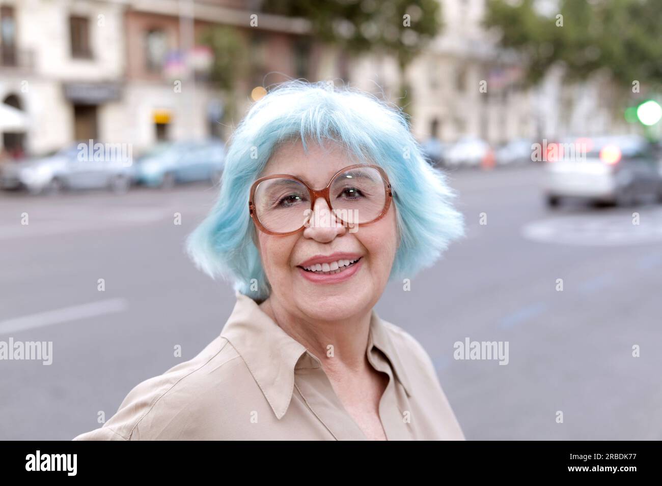 Older blue-haired woman smiling with street in the background Stock Photo