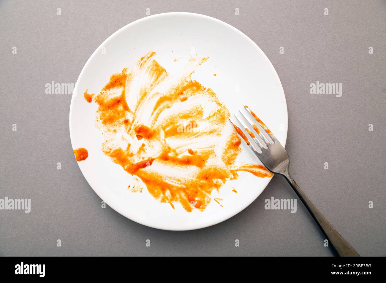 Dirty white ceramic plate with tomato sauce stains, food leftovers and fork, top view Stock Photo