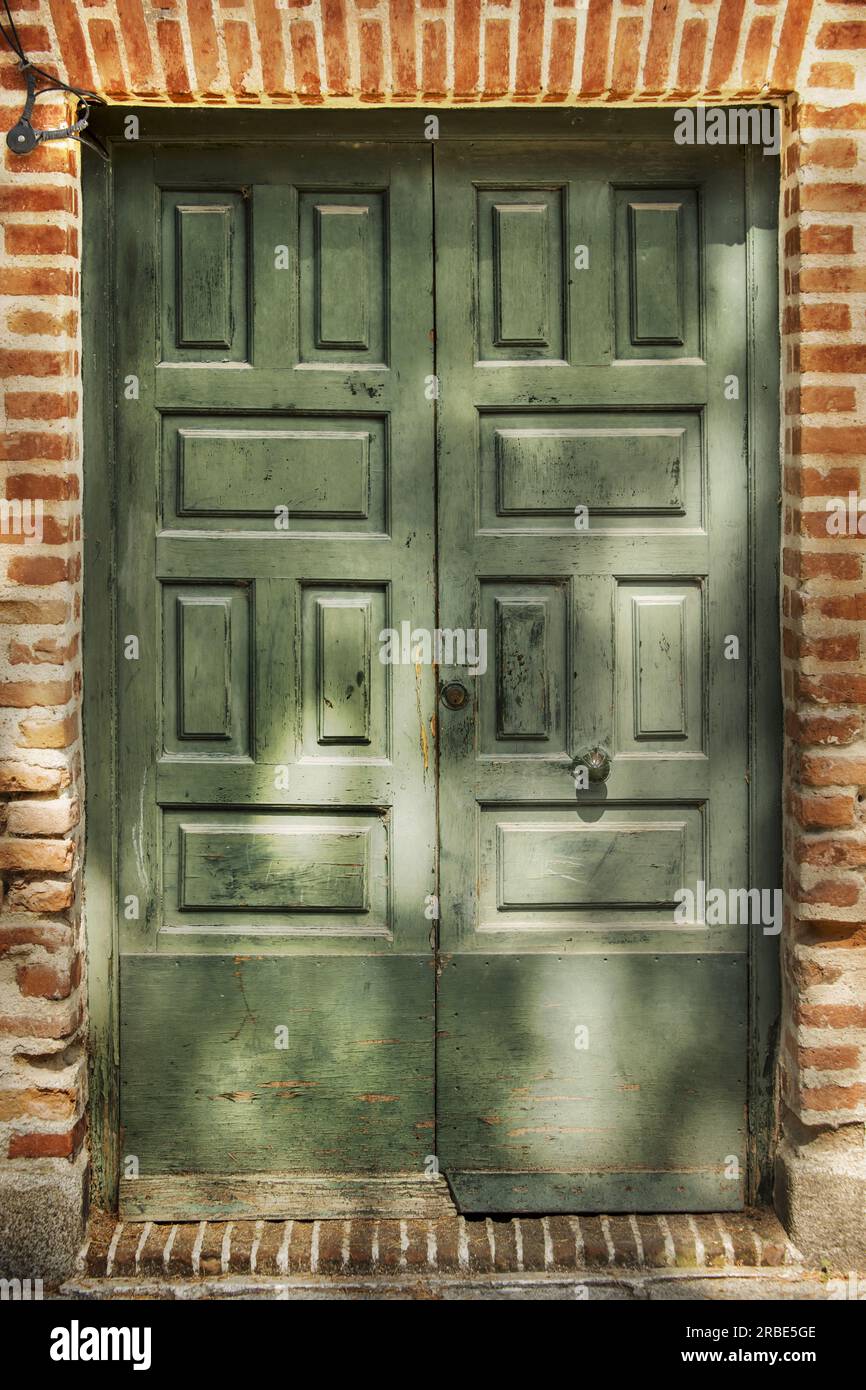 a-green-painted-paneled-wooden-double-door-in-a-brown-brick-driveway