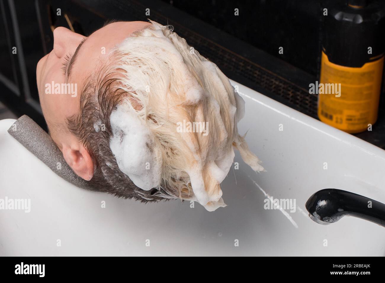 Client's head over sink in foam and soap shampoo in hairdresser before