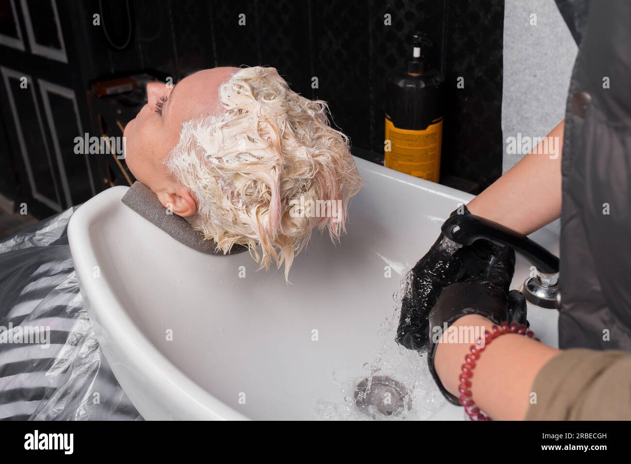 The process of washing hair over the sink to an adult woman in a barbershop or hairdresser. Stock Photo