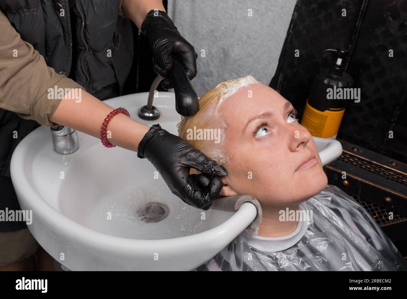 Washing the hair of an adult beautiful woman with rain over the sink at work in a barbershop or hairdresser. Stock Photo