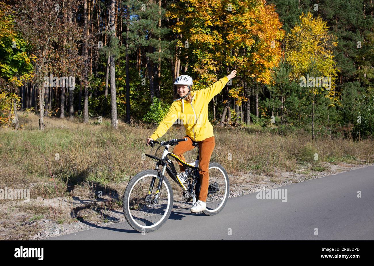 young woman on a bicycle rides in an autumn park on a sunny day. Feeling of freedom and joy. Active lifestyle. having fun on an orange autumn backgrou Stock Photo