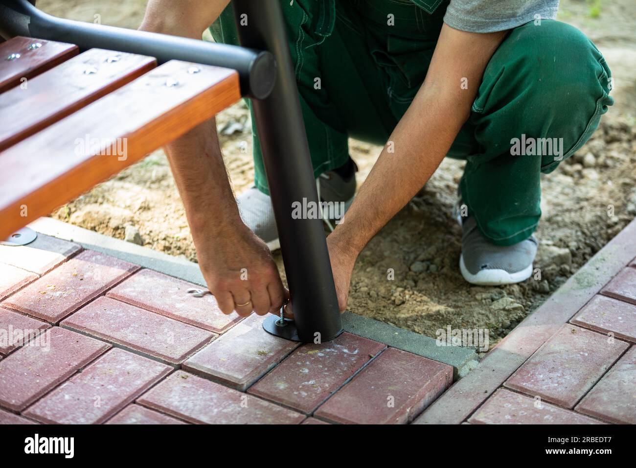 A manual worker bolts the foot of a park bench to paving stones Stock