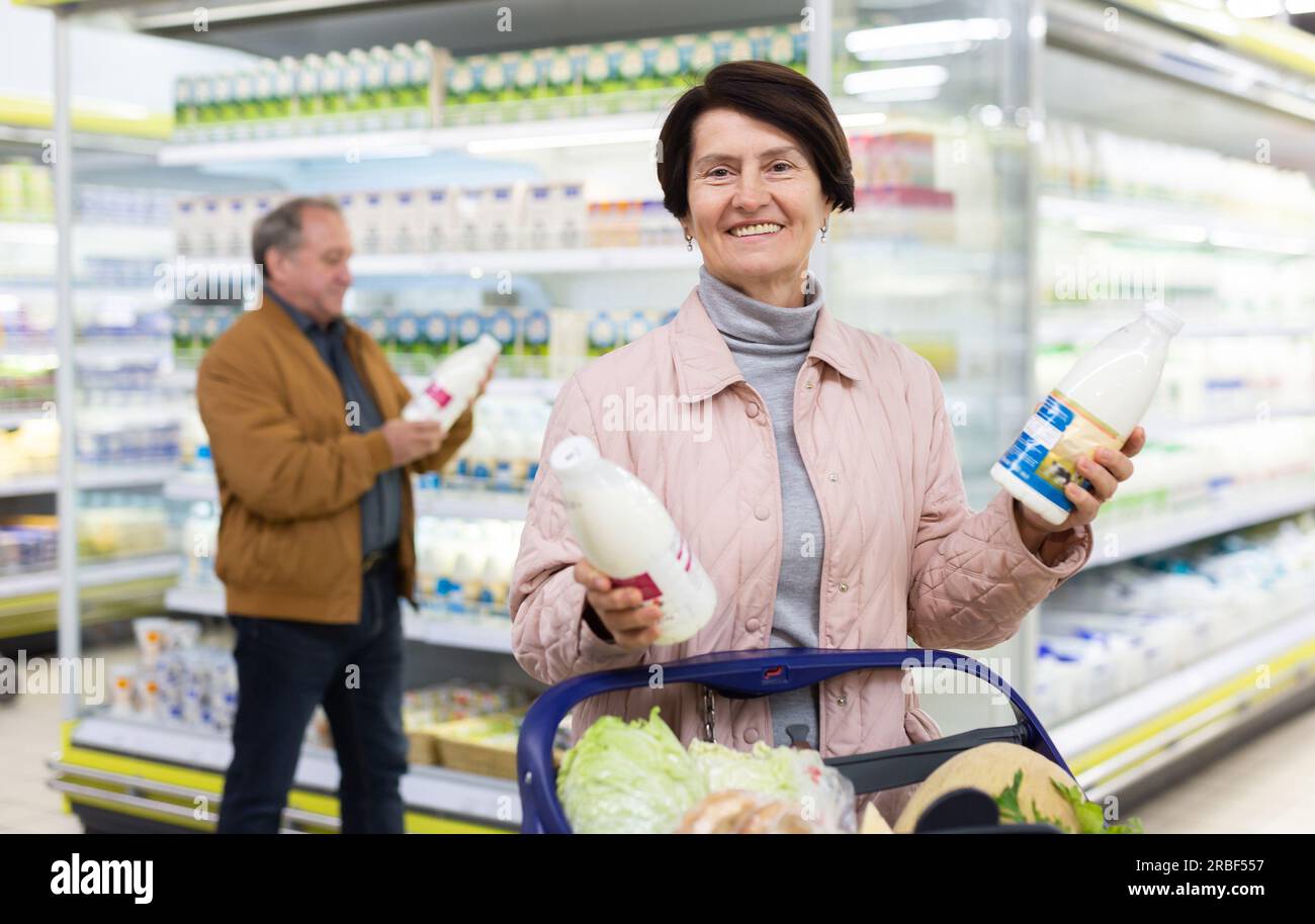 Mature couple choosing jug of milk in dairy department in grocery store