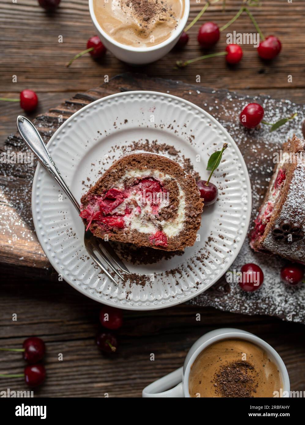 Slice of black forest cake roulade on a plate on wooden background Stock Photo