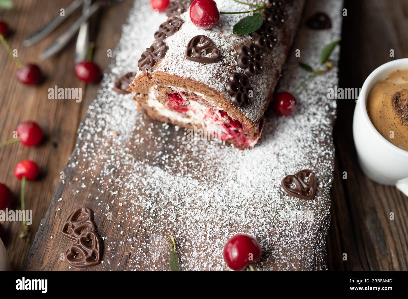 Swiss roll with cream and cherries on wooden background. Delicious chocolate cherry cake roulade Stock Photo