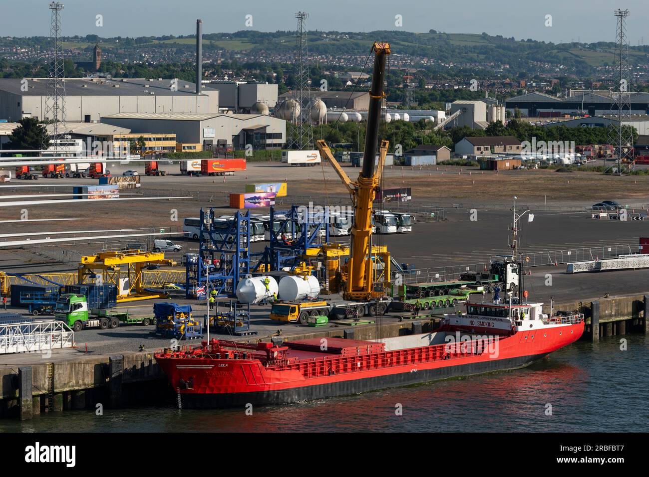 Belfast, Northern Ireland, UK.  7 June 2023.  Red ship with open hatches and a crane unloading turbine blades and equipment relating to wind energy Stock Photo
