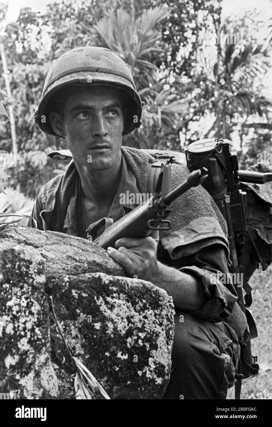 Vietnam:   March, 1968 A 101st Airborne soldier crouches behind a rock as he searches for a sniper in the trees ahead. Stock Photo