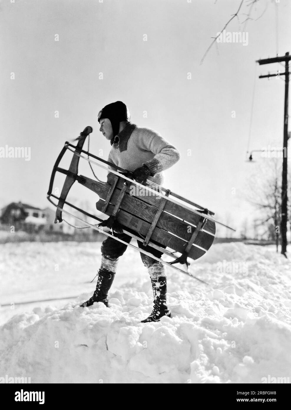 New York:  c. 1935 A boy wearing a leather cap with goggles carrying his sled for a day in the snow. Stock Photo