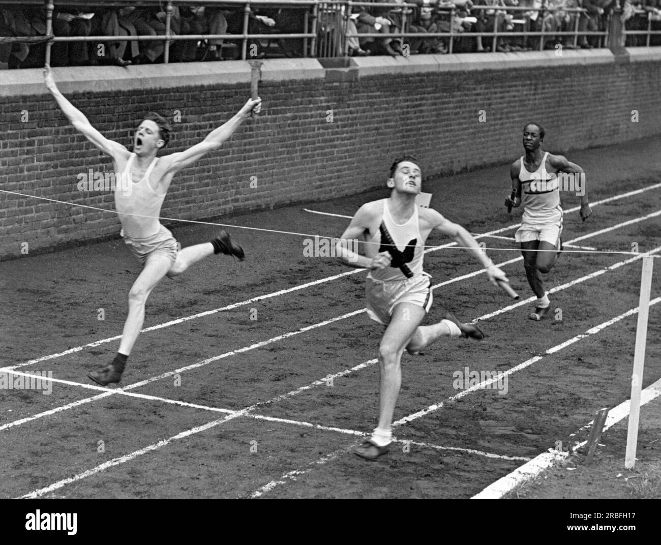Philadelphia, Pennsylvania:  1946 Two runners in the relay event cross the finish line in a dead heat at the Penn Relays Carnival. Stock Photo