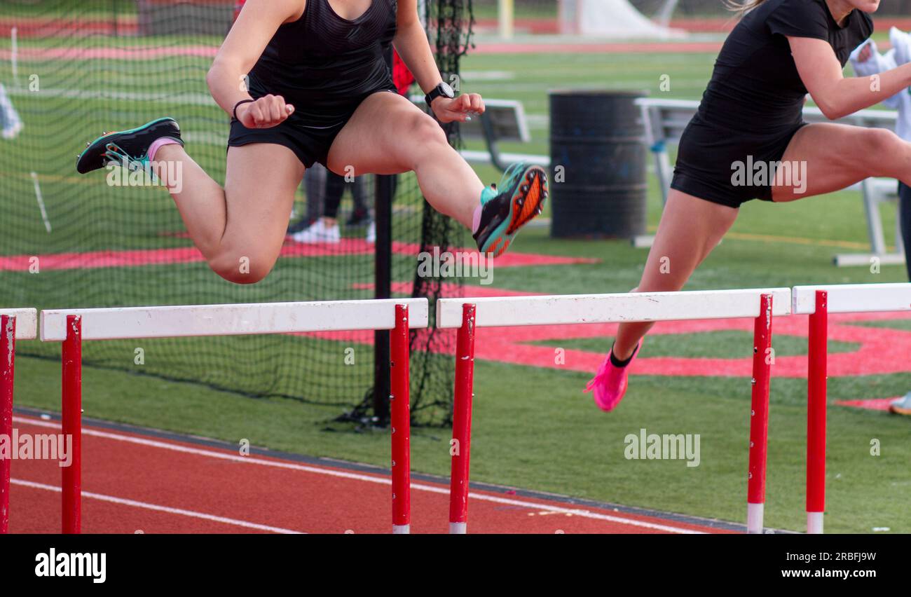 Front view of two high school girls running over hurdles during a track hurdle race outdoors. Stock Photo