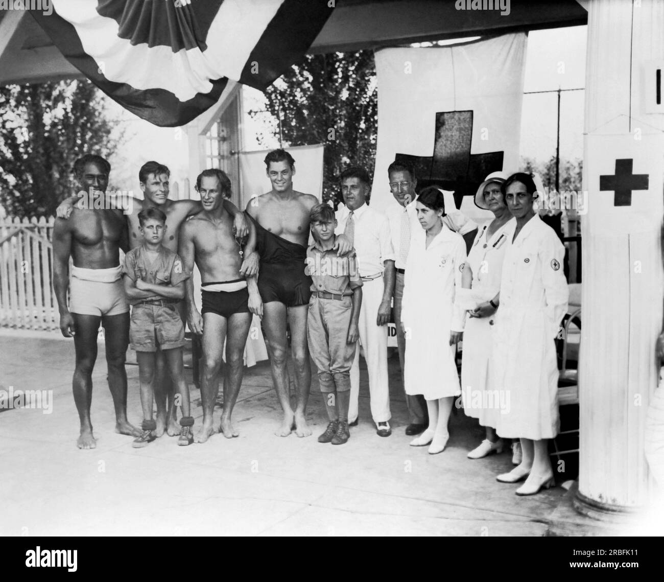 Cincinnati, Ohio:  July, 1932 At the Olympic tryouts are,left to right: Duke F. Kahanamoku, Clarence 'Buster' Crabbe, Harold 'Stubby' Kruger, Johnny Weissmueler, Judge Elmer F. Hunsicker, Paul Goss, Mrs. Mabel Fitzmorris, Mrs. Ella Layne Brown, and Mrs. Carolyn Wayman. Two boy scout messengers stand in front. Stock Photo