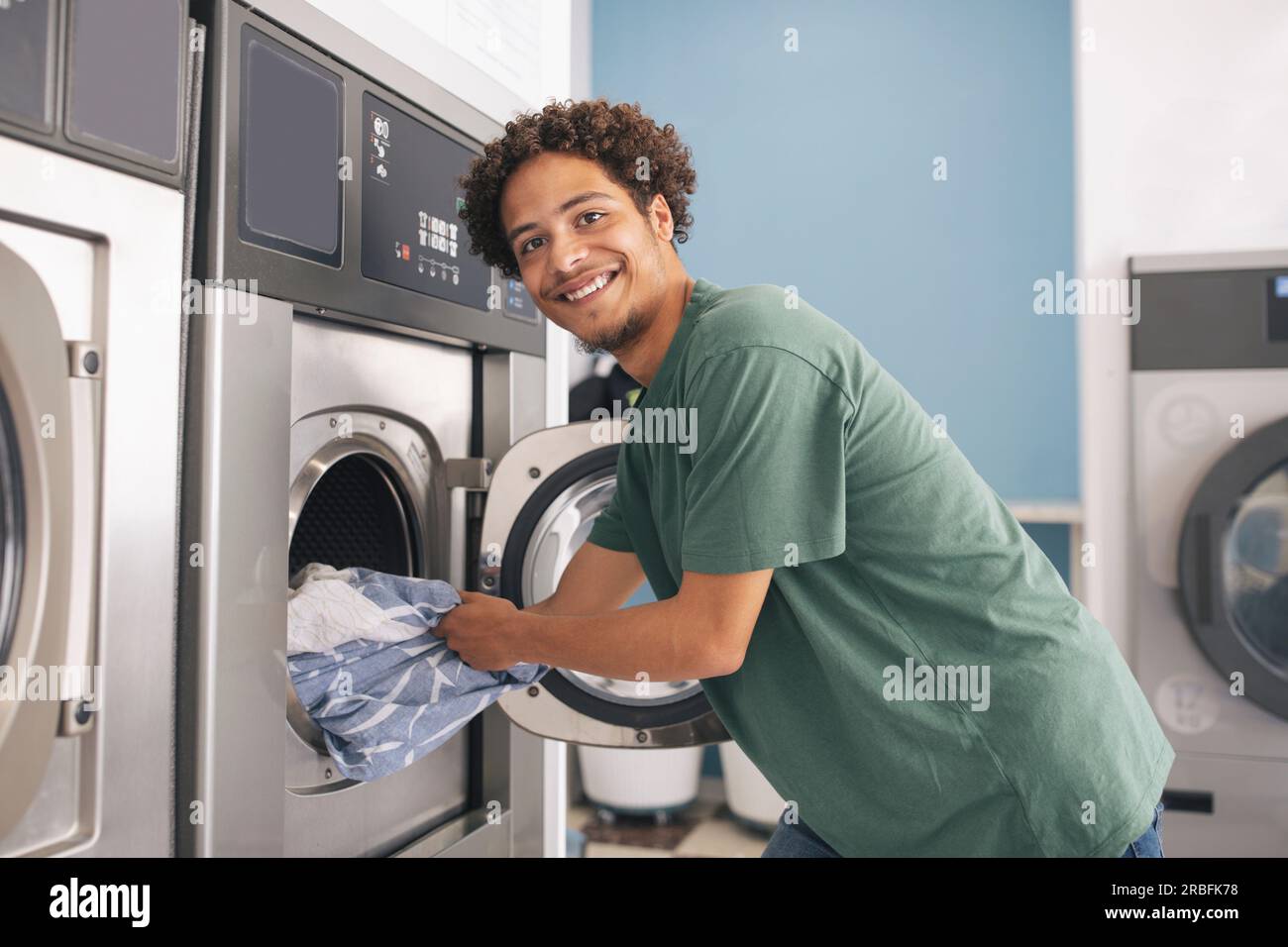 Latin Young Guy Loading Washing Machine Posing At Laundrette Room Stock Photo