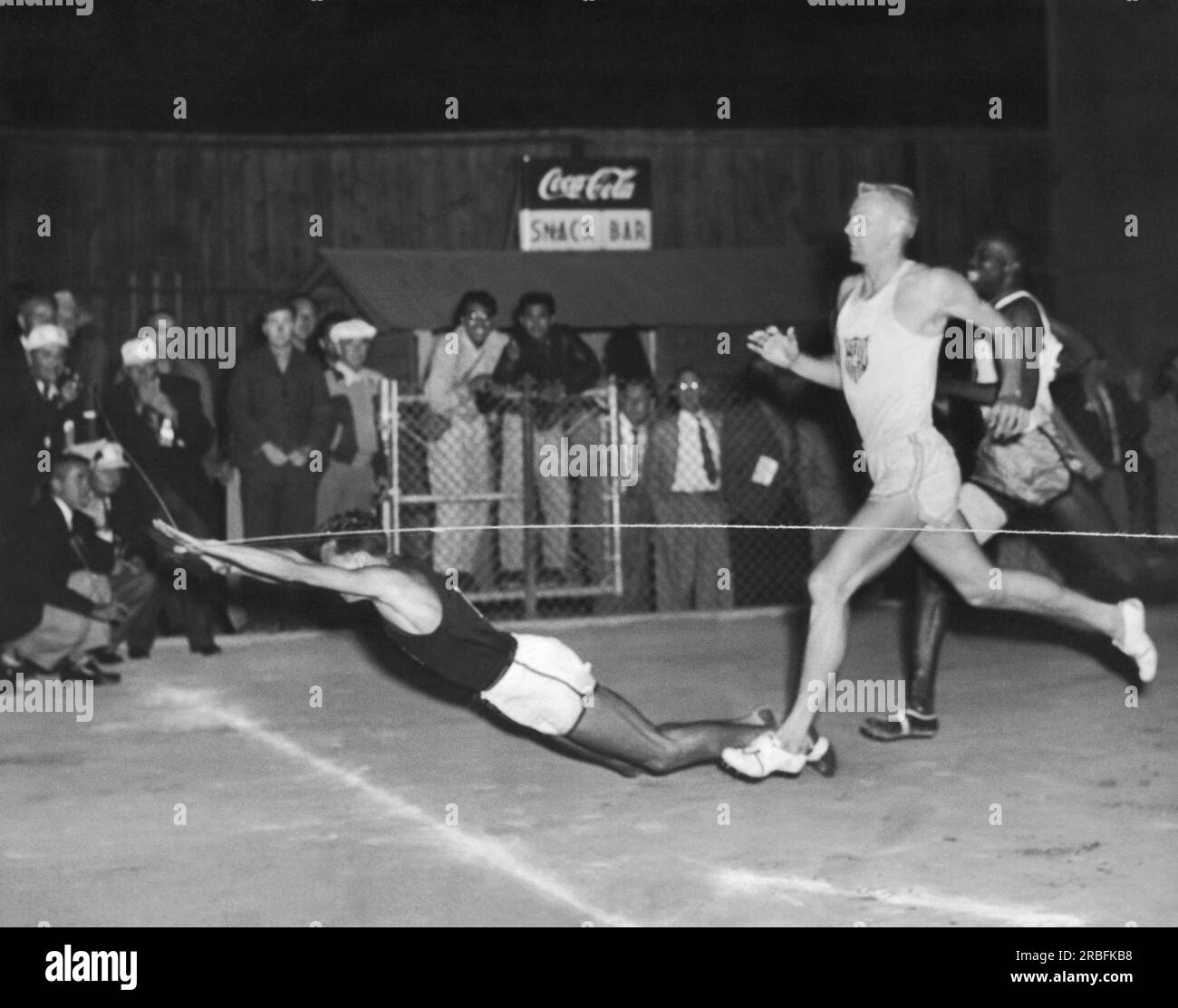 United States:  c. 1948 The lead runner in a race at a track meet falls across the finish line. Stock Photo