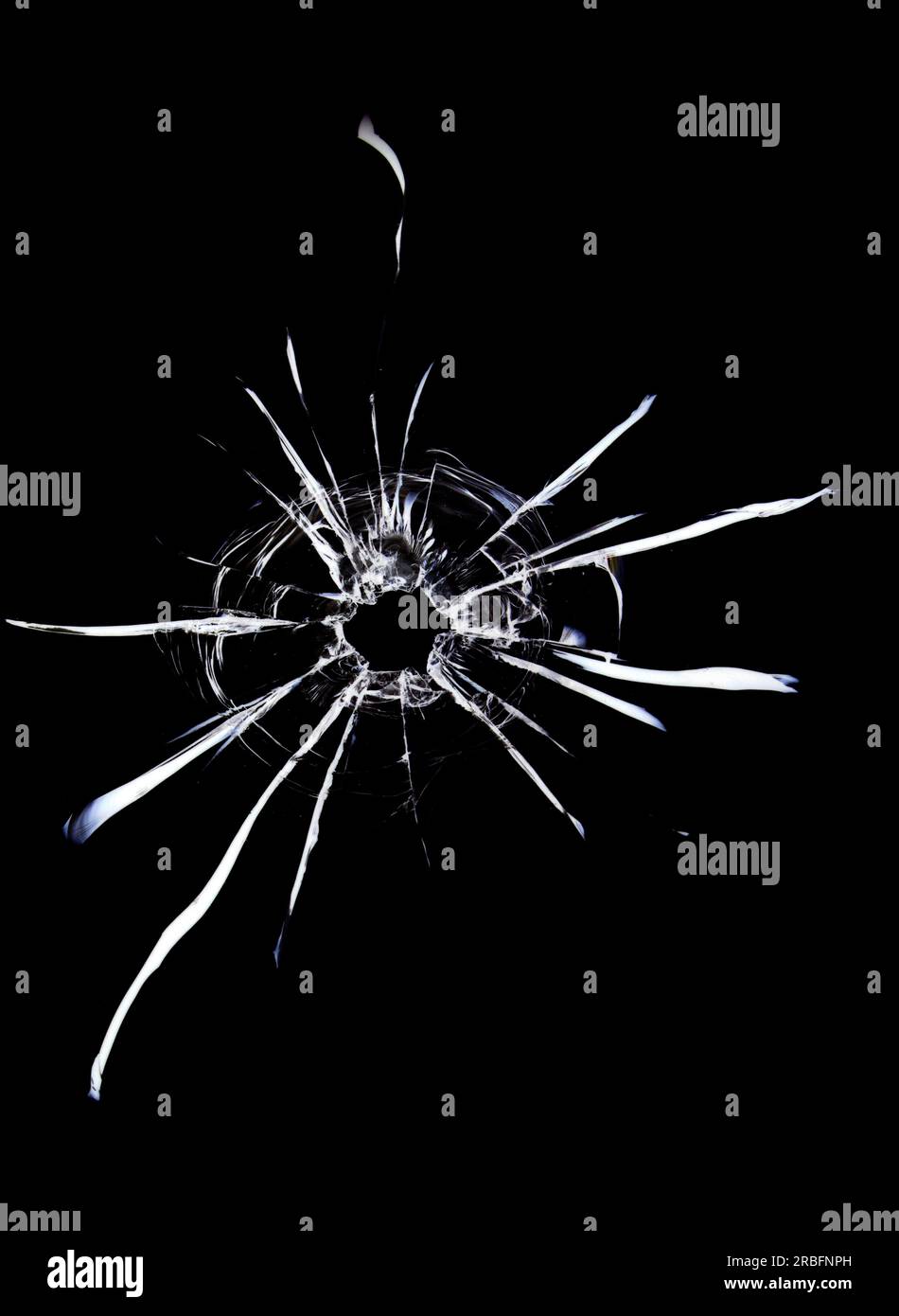 Cracks in the glass on a black background. A bullet hole in a window on a dark background. Stock Photo