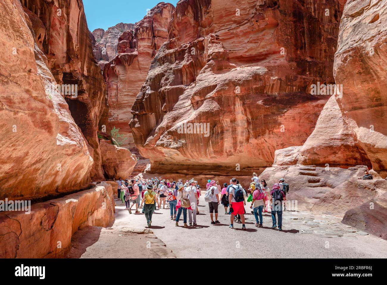 Tourists walk in the Siq, the main entrance to the ancient Nabatean city of Petra, Jordan. Siq is a dim, narrow gorge that ends to the Treasury. Stock Photo