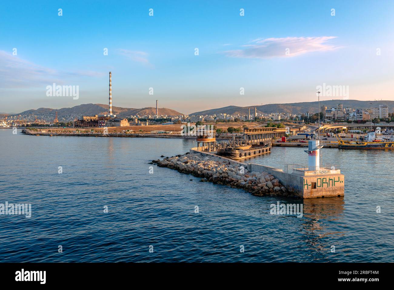 The entrance of the harbor of Piraeus in Greece, with the breakwater and the city of Piraeus with factory smokestacks in the background. Stock Photo