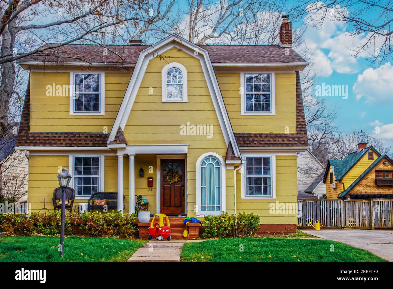 Beautiful yellow house with picturesque roofline and window with childs toy car parked in front - Curb appeal Stock Photo