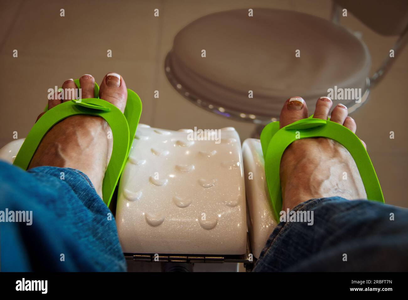 Feet of woman at nail salon who has just had her toes done in the French style and is waiting for them to dry with lime green temporary foam sandals o Stock Photo