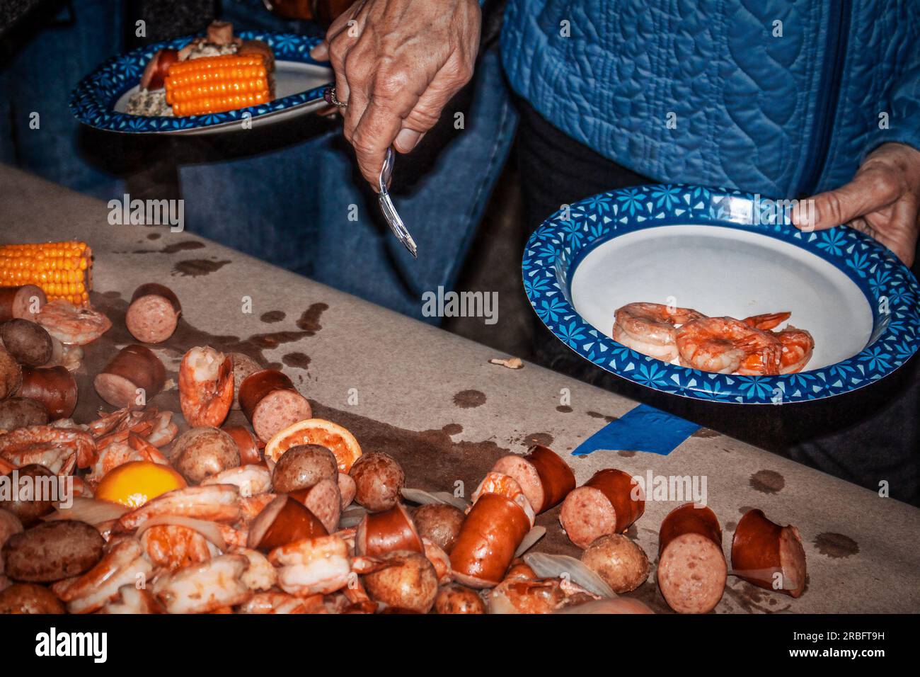 Shrimp and Crawdad boil - food piled on paper taped to table and people in line picking out what they want - paper plates Stock Photo