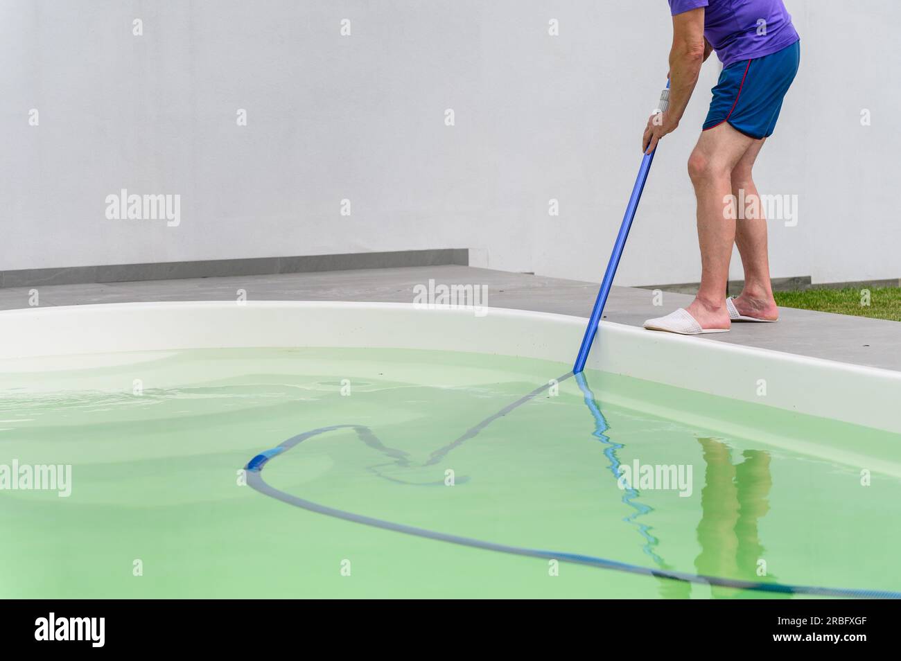 Man cleaning bottom of swimming pool by underwater vacuum cleaner Stock