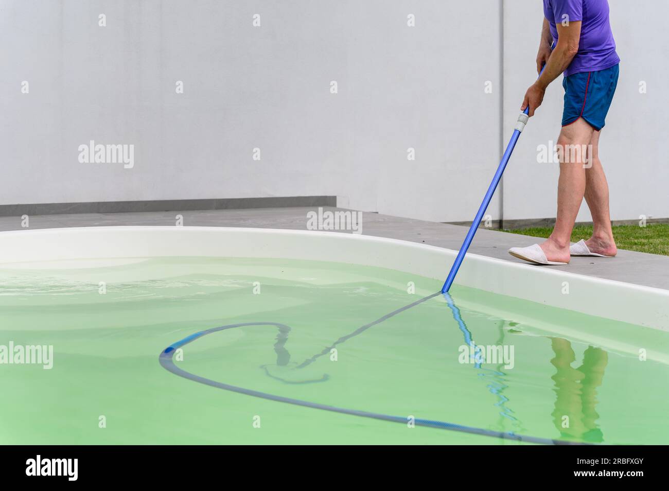 Man cleaning bottom of swimming pool by underwater vacuum cleaner Stock