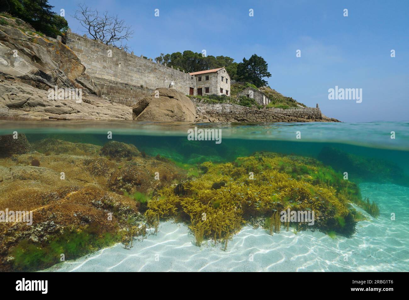 Old house with stone wall and slipway on the ocean shore, Atlantic coast in Spain, split level view over and under water surface, Galicia, Rias Baixas Stock Photo
