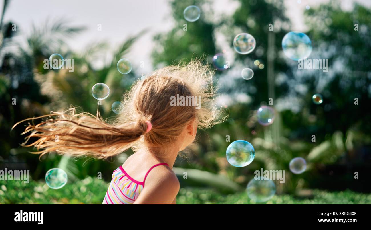 Back view of happy little girl playing soap bubbles on the nature. Childhood, lifestyle concept Stock Photo